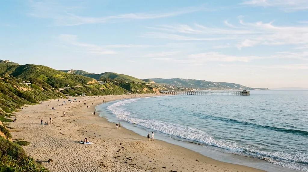 A calm Southern California beach with a pier and green hills in April.
