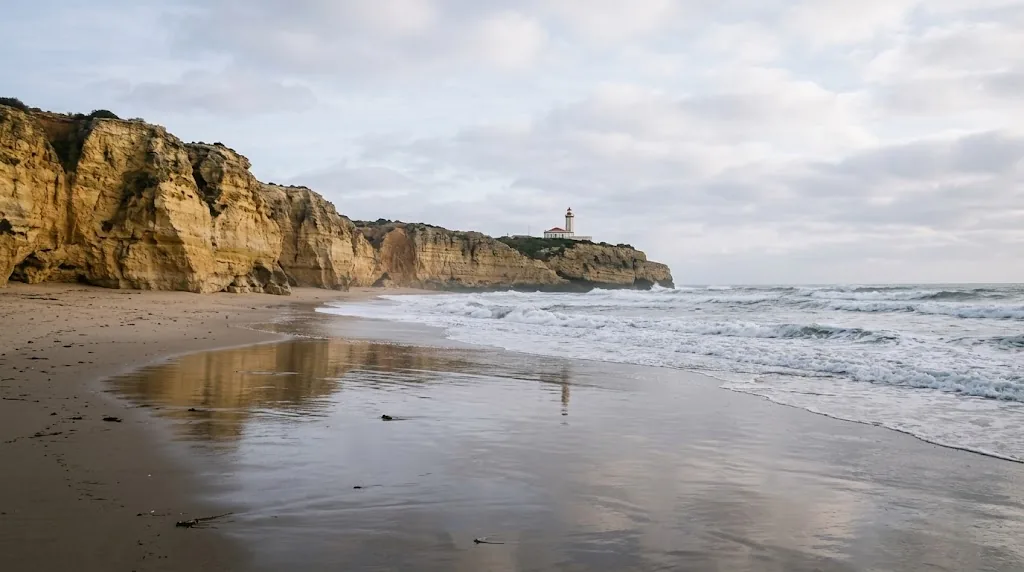 A quiet Portuguese Atlantic beach in winter with golden cliffs and a lighthouse.